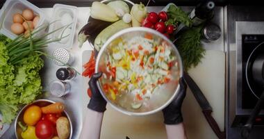 A woman in disposable black gloves mixes salad in a bowl without using cutlery, close-up of her hands, top view video