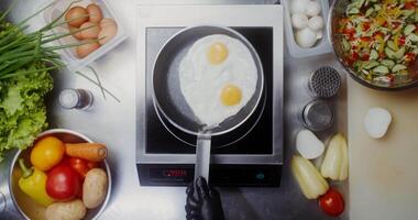 A woman in disposable black gloves adds seasonings to eggs frying in a frying pan, close-up of her hands, top view video