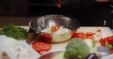 A woman in a chef's uniform with disposable black gloves on her hands puts chopped vegetables in a bowl standing in the restaurant kitchen, close-up of hands video
