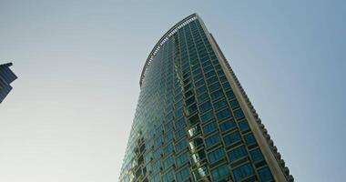 View from below, the facade of a glass skyscraper of unusual shape against a clear blue sky video