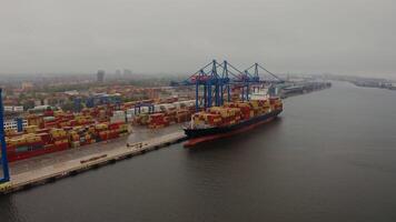 A barge loaded with containers for international maritime transport stands in an industrial port, Klaipeda, Lithuania. Drone . video