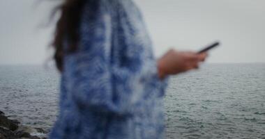 A woman is typing on a mobile phone while standing on the rocks on the seashore. Close-up of female hands, no face. 4k , red komodo video