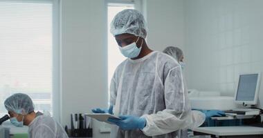 An African-American male laboratory assistant looks up from using a digital tablet and looks directly at the camera while working in a modern laboratory. 4k , red komodo video