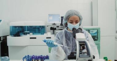 A female laboratory assistant in sterile disposable clothing places a plasma sample on a microscope slide with a pipette and performs an analysis, front view. 4k , red komodo video