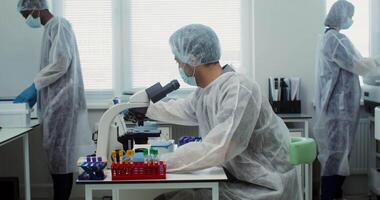 A male laboratory assistant places biological material on a microscope slide for further study while working as a team in a modern laboratory. 4k , red komodo video