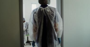 A female laboratory assistant in disposable sterile clothes enters a modern laboratory passing by working colleagues, bringing in a box with test samples. 4k , red komodo video