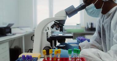 A young African American laboratory assistant checks the patient's tests using a microscope. Close-up, details of work in a modern laboratory. 4k, red komodo video