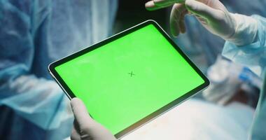 Doctor surgeon uses a tablet in the operating room. Close-up of a tablet with a green screen in rubber-gloved hands. Chromakey, layout, copy space. in 4k, red komodo video