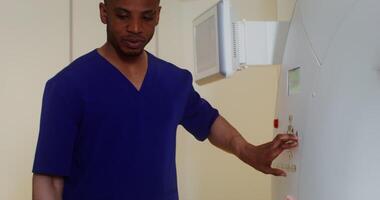 A young male doctor of African American appearance smiles and talks to a patient lying on an MRI machine, pressing a button on the machine's control panel, close-up. in 4k, red komodo video