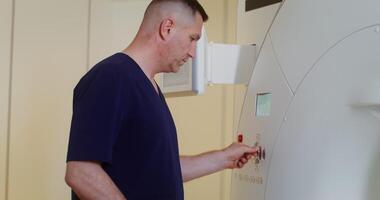 An adult male doctor operates a CT scan machine by pressing a button on the control panel, performing an MRI scan on a young female patient in a modern clinic. in 4k, red komodo video