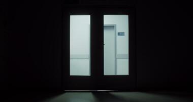 Medical workers run down the hallway pushing a medical gurney with an urgent patient. filming from a dark corridor through a glass door. in 4k, red komodo video