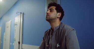 Frustrated tired young doctor cries in the corridor of the medical center, covering his eyes with his hands. in 4k, red komodo video