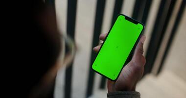 une mobile téléphone avec une vert écran dans le main de une homme avec lunettes, fermer, tournage de derrière, le visage est ne pas visible. copie espace, maquette, chrominance clé. dans 4k, rouge Komodo video