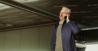 A respectable gray-haired man of European appearance, dressed in a coat, is talking on a mobile phone while walking through an underground parking lot. in 4k, red komodo video