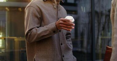 Serious African American man with a disposable cup of coffee in his hand talking with his interlocutor while standing outdoors, close-up, motion to the man's face. in 4k, red komodo video