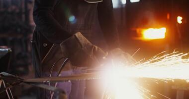 African American man dressed in work clothes and goggles with a concentrated uses a plasma cutter, cutting a sheet of iron, while working in forge. Close-up, motion to the face. 4k, red komodo video