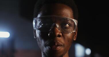 Young African-American man in goggles smiling looking at the camera while standing in a modern forge, close-up of a man's face. 4k, red komodo video
