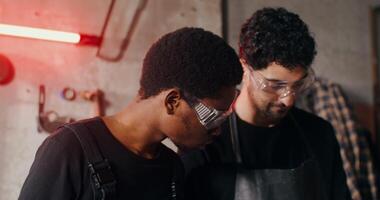 Two blacksmiths of different nationalities in work clothes are considering a sketch of a future product, working together and using a tablet, close-up. 4k , red komodo video