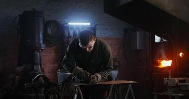 A young man of European appearance, dressed in work clothes and goggles, cuts a sheet of iron with a plasma cutter, working in a forge, sparks fly in different directions. 4k, red komodo video