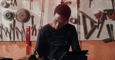 African American man in protective gear uses a digital tablet to draw a sketch of a future product while working in a workshop, close-up. in 4k, red komodo video