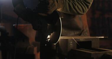 A blacksmith in protective equipment saws off a part of a metal stick using a flex, metal sparks fly in different directions, close-up, no face, unrecognizable person. 4k , red komodo video