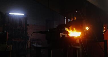 A blacksmith in protective gear and goggles takes an angle grinder and starts to cut off a part of a metal blank while working in a forge. 4k , red komodo video
