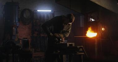 A blacksmith in protective gear and goggles saws off a part of a metal blank using a flex, metal sparks fly in different directions. 4k , red komodo video