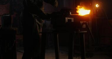 A blacksmith in protective gear and goggles cuts a metal pole with an angle grinder, bright sparks fly in all directions. in 4k, red komodo video