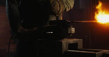 A blacksmith in protective equipment saws off part of a metal stick using an angle grinder, metal sparks fly in different directions, close-up, no face, unrecognizable person. 4k , red komodo video