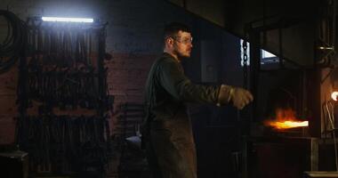 The blacksmith places a metal billet in a burning furnace and, after closing the valve, waits for the iron to melt. Blacksmith workplace, iron forging workflow. 4k , red komodo video