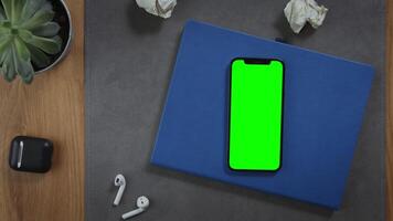 A man puts a cup of hot coffee on the desktop next to a mobile phone with a green screen lying on a notebook with crumpled pieces of paper nearby, close-up. Mockup, chroma key, copy space video