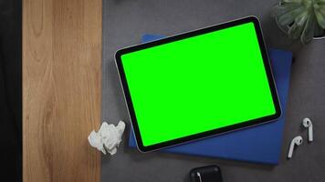 A man puts a cup of tea on the desktop next to a digital tablet with a green screen lying on a notepad with crumpled pieces of paper nearby, top view, close-up. Mockup, chroma key, copy space video