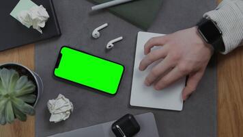 A man's hand lies on a blank sheet of notebook, next to a mobile phone with a green screen and crumpled sheets of paper, then takes the headphones, close-up. Mockup, chroma key, copy space video