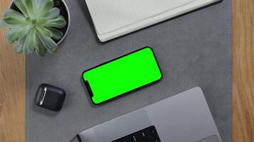Close-up of male hands putting wireless headphones next to mobile phone with green screen to desktop, unrecognizable person. Mockup, chroma key, copy space video