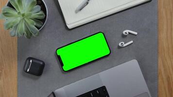 A man takes wireless headphones lying next to a smartphone with a green screen from the desktop, Close-up of male hands, unrecognizable person. Mockup, chroma key, copy space video