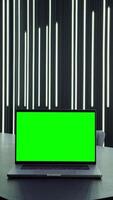 Young businesswoman uses a tablet while walking near the desktop with an open laptop with a green screen standing on it, vertical . Chroma key, mockup, copy space. in 4k format, red komodo. video
