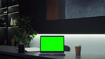 An open laptop with a green screen stands on desk of a businesswoman using a tablet with a serious look while walking behind in a stylish office. Chroma key, copy space. in 4k format, red komodo video