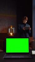 An open laptop with a green screen stands on a desktop in the office of a young businesswoman using a tablet. Mockup, chroma key, copy space. in 4k format, red komodo. video