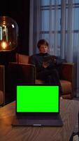 An open laptop with a green screen stands on a desktop in the businesswoman's office using a tablet while sitting in a chair. Mockup, copy space, vertical . in 4k format, red komodo. video