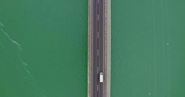 View from above, a narrow road bridge with cars passing over it, over a river with green water with small ripples of waves. recording from a quadcopter video