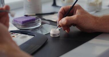Coating a ceramic denture with a fine brush by hand. Close-up of the hands of an orthodontist, the man's face is not visible. in 4k, red komodo video