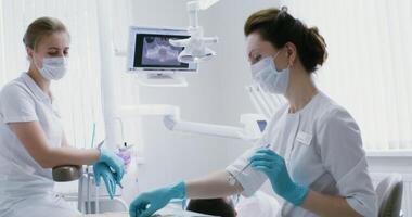A woman dentist in disposable rubber gloves takes instruments from the table and examines the patient's oral cavity. Sanitation of the oral cavity in a modern dental clinic. in 4k, red komodo video