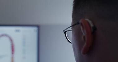 Close-up of part of the head of a man in glasses, looking at a screen with a blurry image, sitting in darkness, rear side view. in 4k, red komodo video
