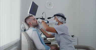 A female otorhinolaryngologist examines the sinuses and nose of a patient using a medical mirror. Preventive examination of the respiratory system. in 4k, red komodo. video