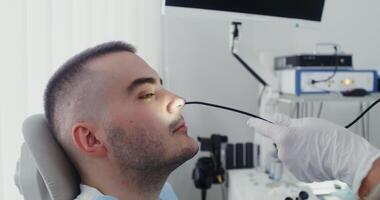An otorhinolaryngologist inserts a tube with a mini camera into the nose of a male patient to conduct an examination of the nasal cavity. in 4k, red komodo. video