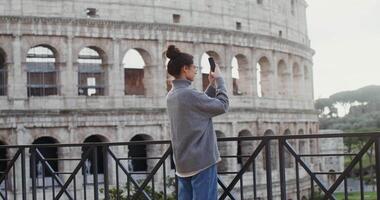 A young beautiful woman taking photos of the sights of Rome on a mobile phone, standing on an observation deck near the Coliseum. in 4k, red komodo. video