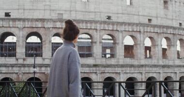 A young beautiful woman of European appearance smiles while taking photos of the sights of Rome on a mobile phone, standing on an observation deck near the Coliseum. in 4k, red komodo. video