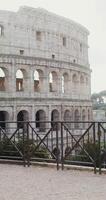 A young warmly dressed woman comes to the observation deck in front of the Coliseum and stops looking at the amphitheater. Italy Rome. in 4k, red komodo, vertical video