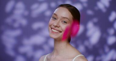 Beautiful young Caucasian model without makeup, with tied hair, smiling broadly looking into the camera while standing against the background of falling rose petals in the studio. 4K , red komodo video