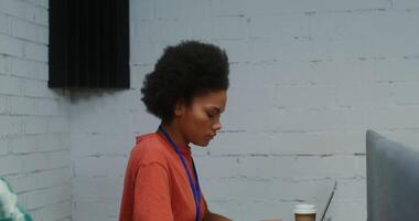 A young beautiful African American woman uses a laptop, working at the same desk with a partition in front of a young Asian man, from the side. 4K , red komodo video